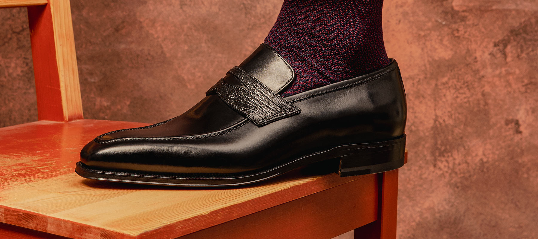 Black Calf and Black Shark Penny Loafers with Burgundy socks displayed on a chair